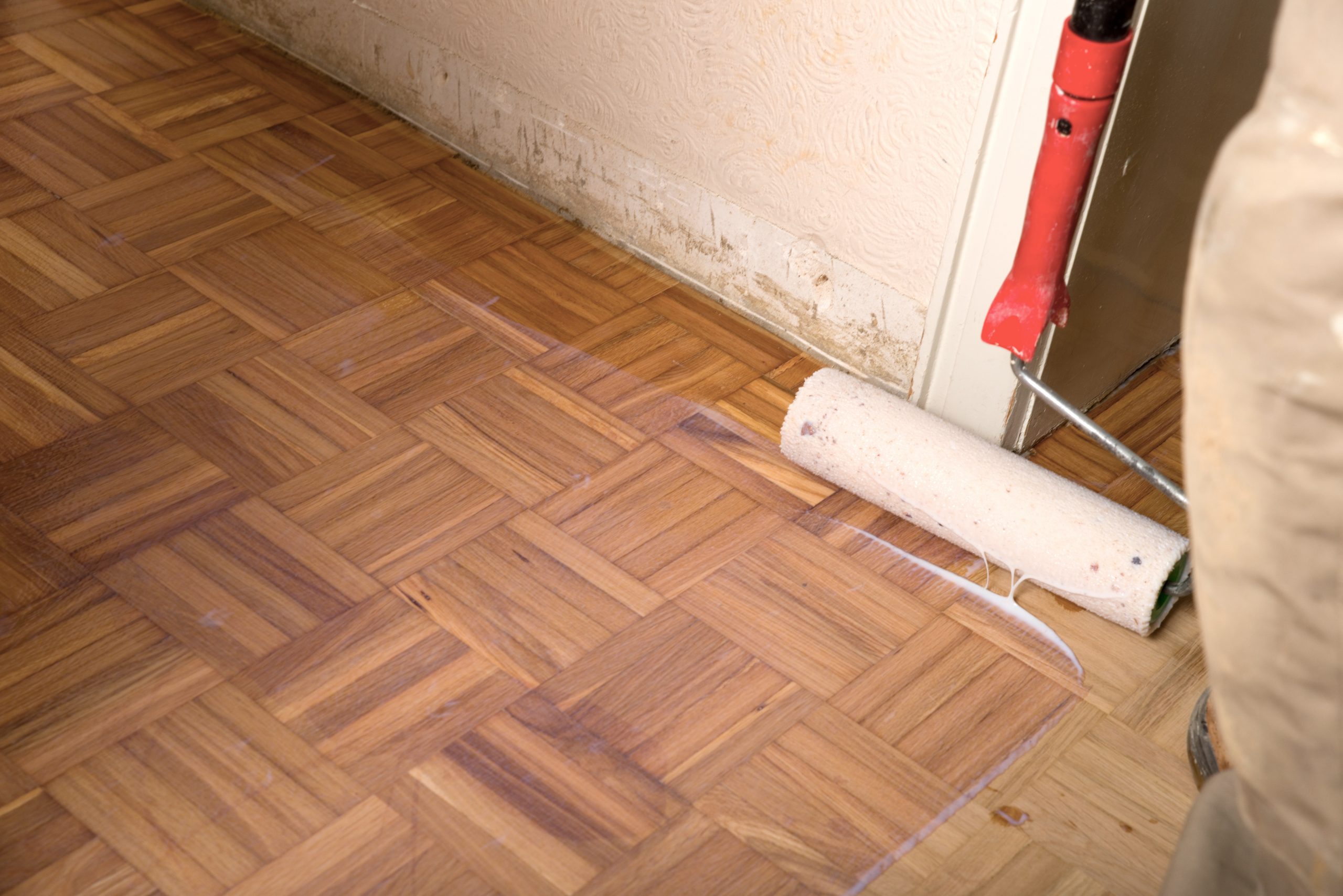 Expert Wood Floor Sanding in Hounslow—contractor using a paint roller to apply clear lacquer to a newly sanded oak mosaic parquet floor.