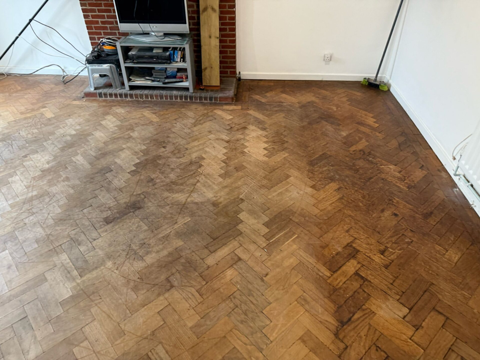 Parquet Floor Restoration in Hounslow showing a heavily worn oak herringbone parquet wood floor in a living room before sanding and refinishing.