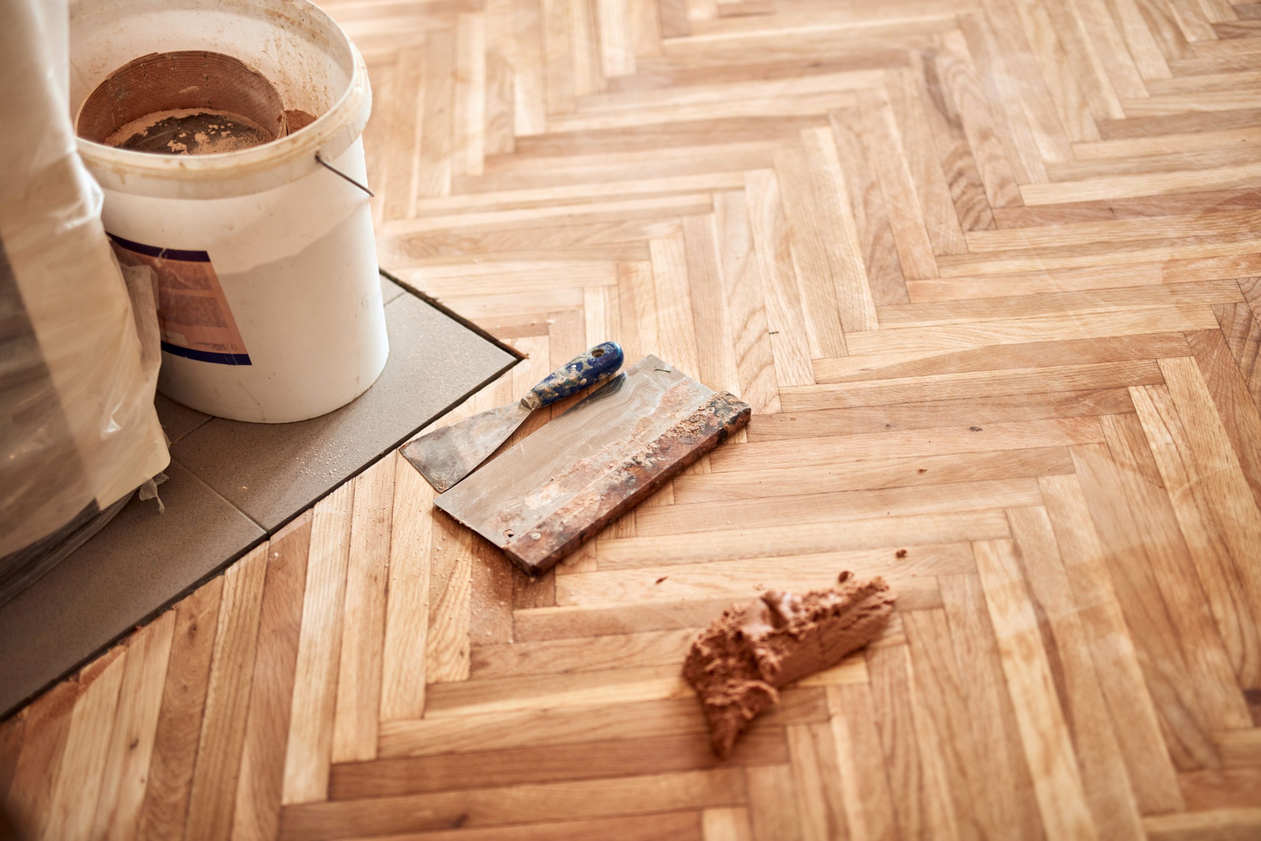 Parquet Floor Restoration in Hounslow with gap filling on a sanded herringbone oak parquet wood floor using resin and filler tools.