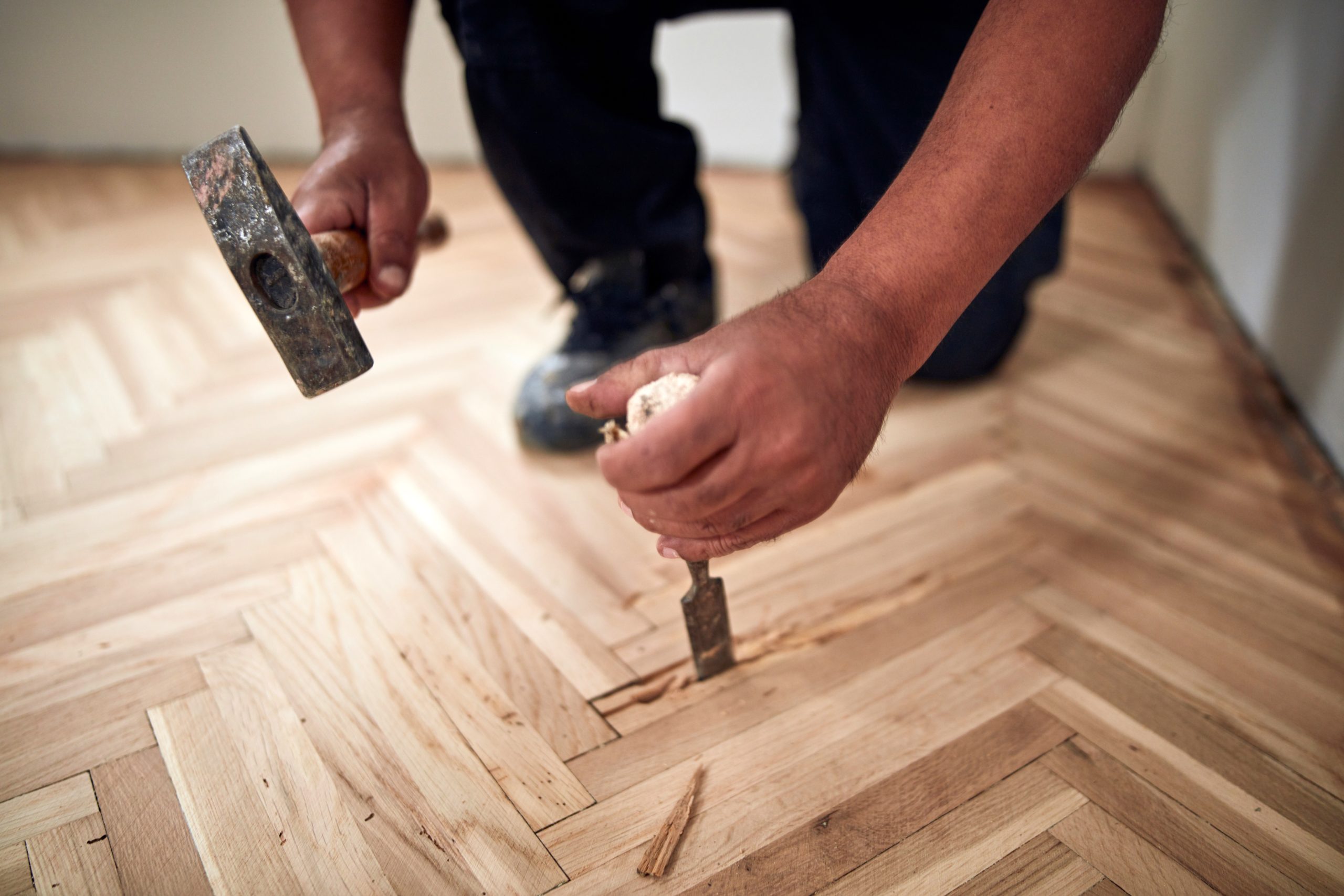 Parquet Floor Restoration in Hounslow with a technician repairing damaged herringbone oak parquet wood floor blocks using a hammer and chisel.