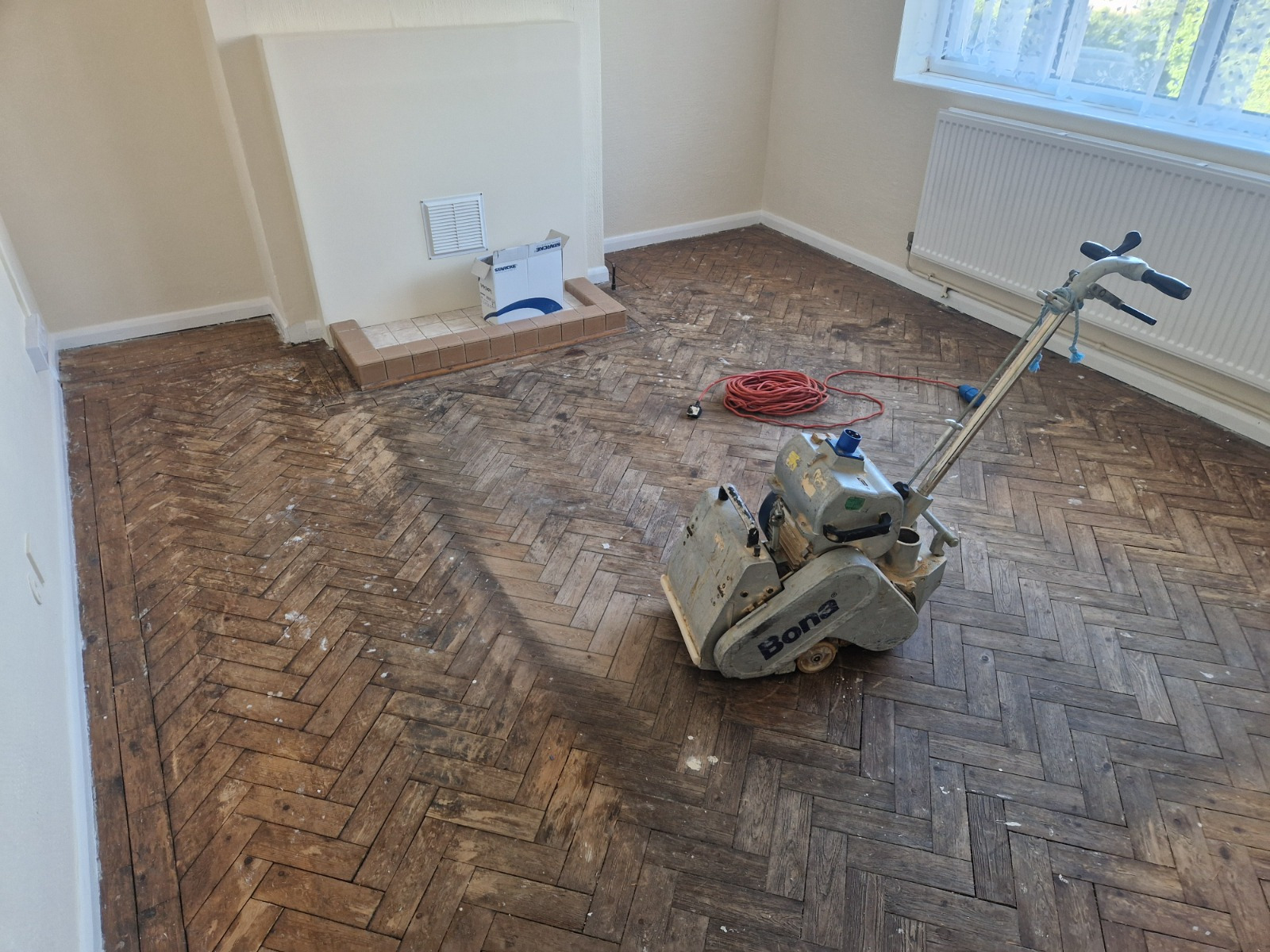 Parquet Floor Restoration in Hounslow with a professional Bona sander on a herringbone oak parquet wood floor in a living room mid-sanding.
