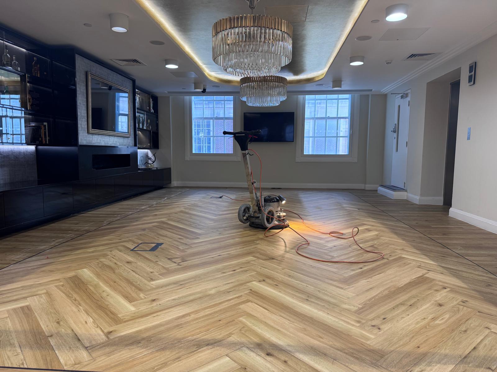 Parquet Floor Restoration in Hounslow showing a large modern lounge with a light oak herringbone parquet wood floor being polished by a professional rotary floor sanding machine.