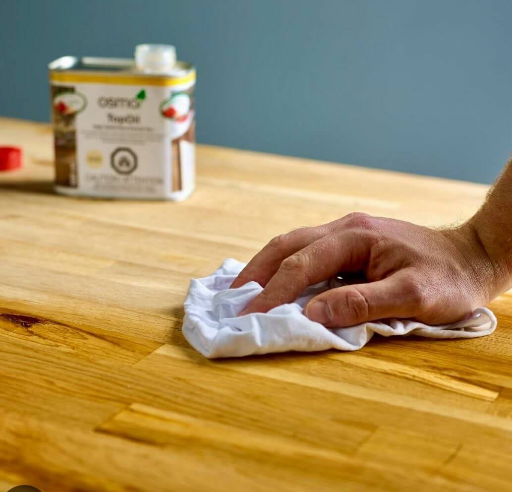 Worktop Refinishing in Hounslow – hand wiping oil onto an oak butcher-block kitchen worktop above an engineered oak floor for a smooth, protected finish.