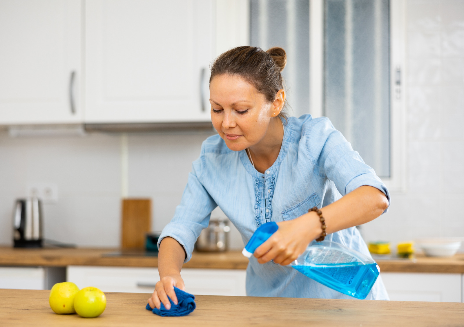 Woman cleaning an oak wooden kitchen worktop after Worktop Refinishing in Hounslow, with a matching oak hardwood floor in the background.