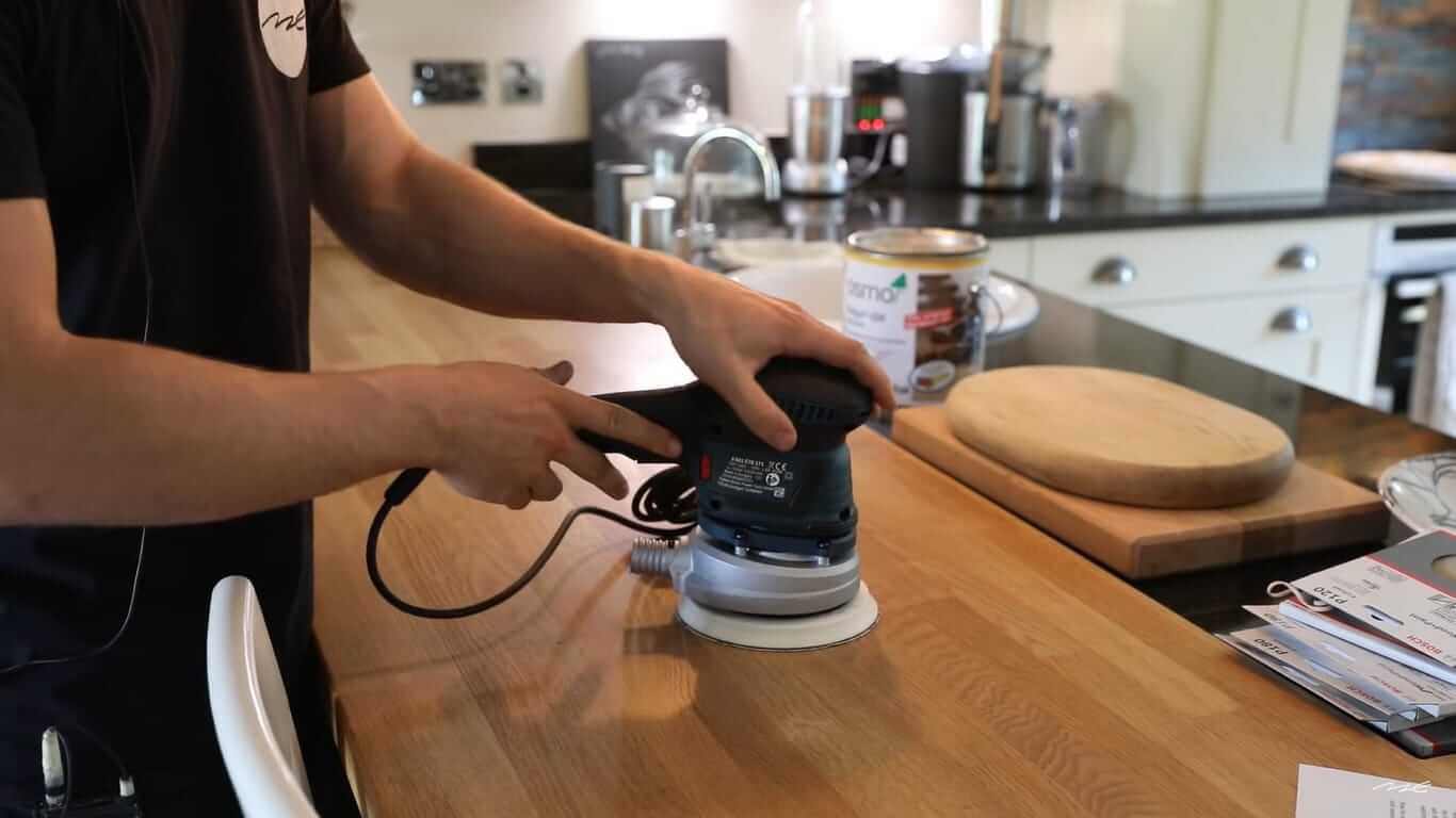 Professional Worktop Refinishing in Hounslow – tradesperson sanding a solid oak kitchen worktop with an electric sander above an oak plank floor.