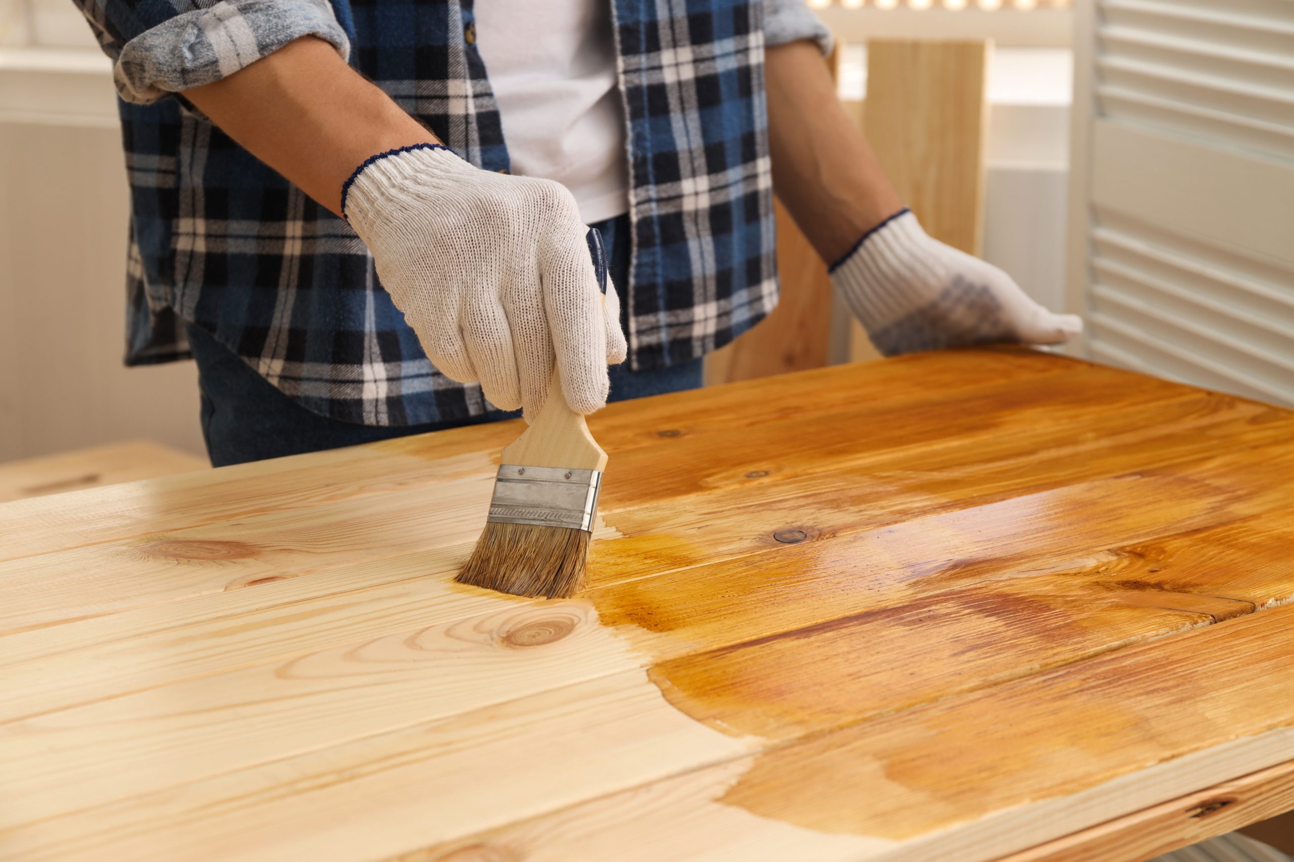 Worktop Refinishing in Hounslow – tradesperson applying stain to a solid pine wood kitchen worktop with matching pine floorboards for a rich, warm finish.