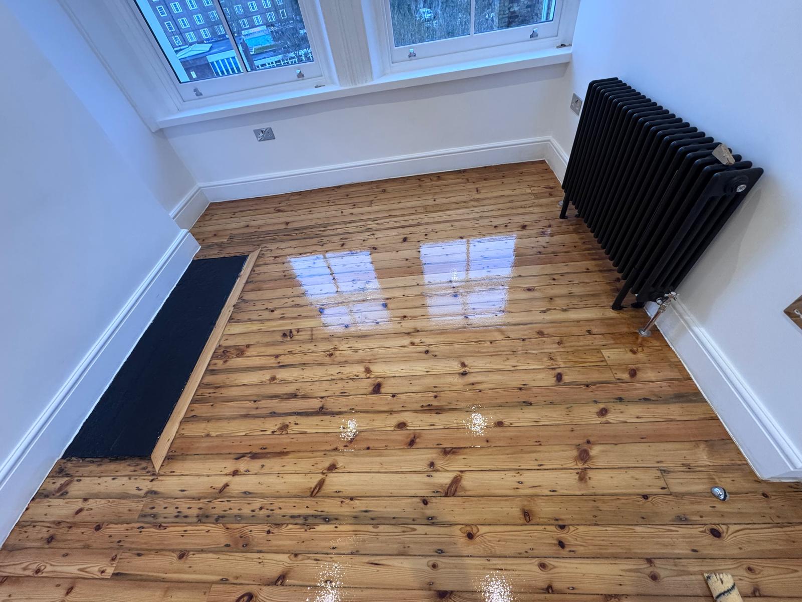 Wood Floor Sanding in Hounslow showing gloss-finished pine softwood floorboards with a bright, reflective sealed surface after professional sanding and finishing.