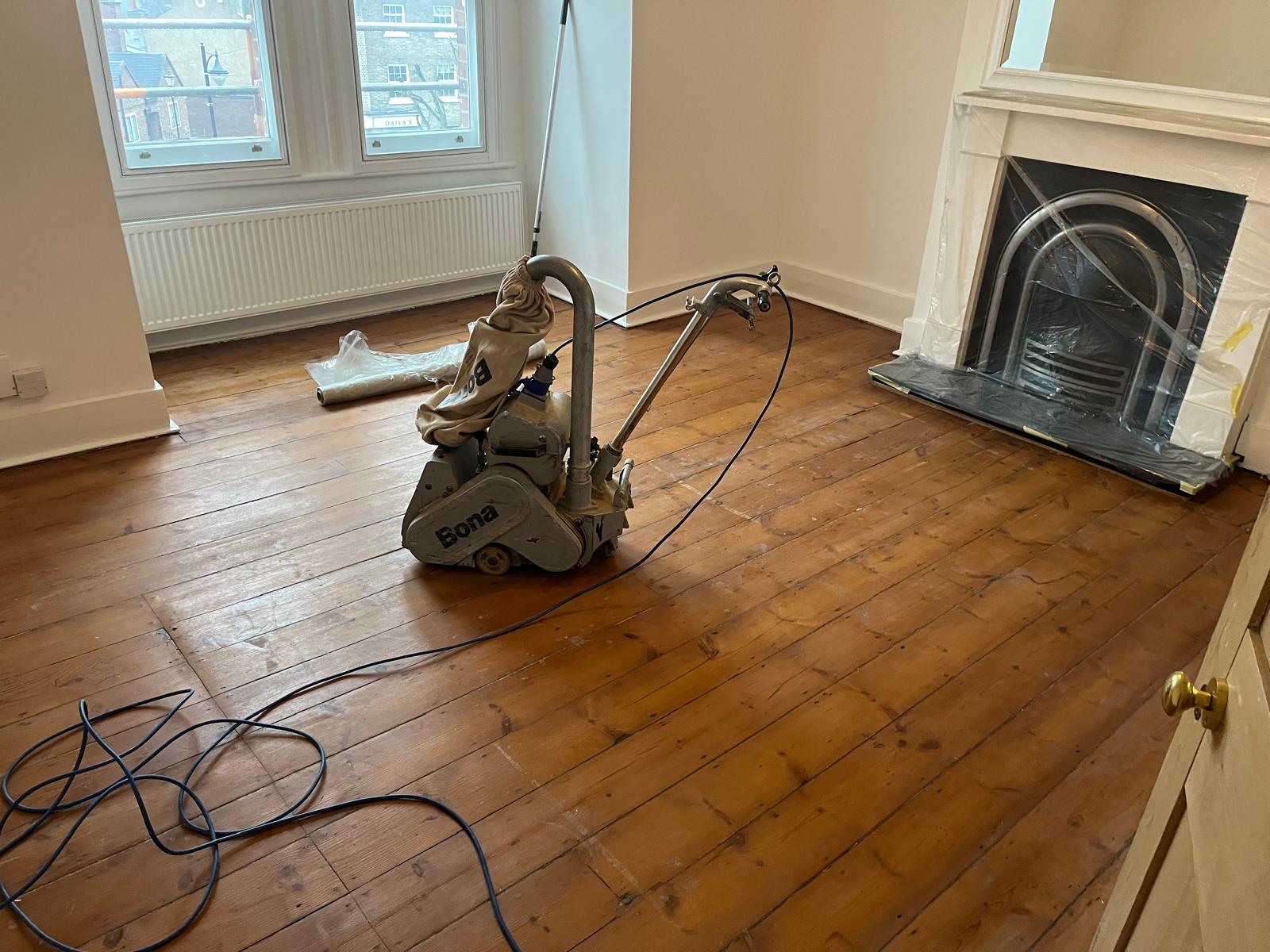Wood Floor Sanding in Hounslow on original pine floorboards in a living room, with a professional Bona floor sander restoring worn timber boards.